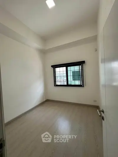 Spacious empty room with large window and wooden flooring, perfect for customization.