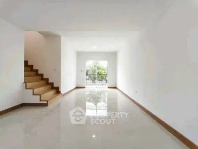 Spacious modern living room with glossy tiled floors and staircase, leading to a bright balcony view.