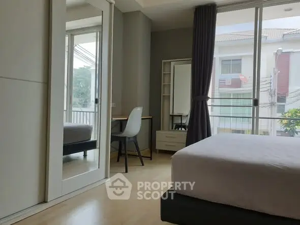 Modern bedroom with large window and study area, featuring sleek furniture and natural light.