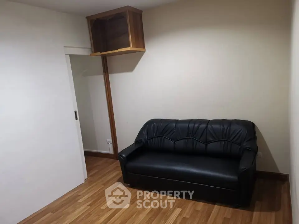 Cozy small living room with black leather sofa and wooden flooring