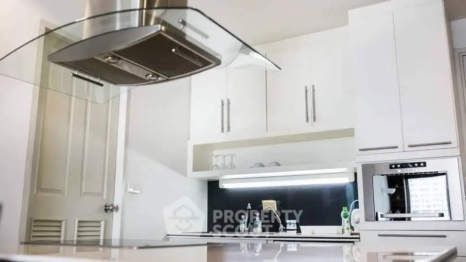Modern kitchen with sleek white cabinets and built-in oven, featuring a stylish range hood.