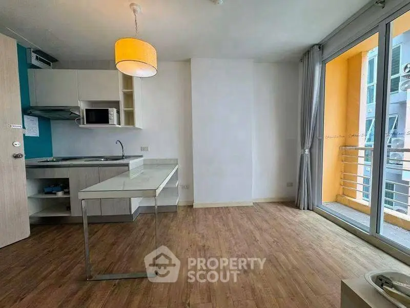 Modern apartment with open kitchen and balcony, featuring wooden flooring and ample natural light.
