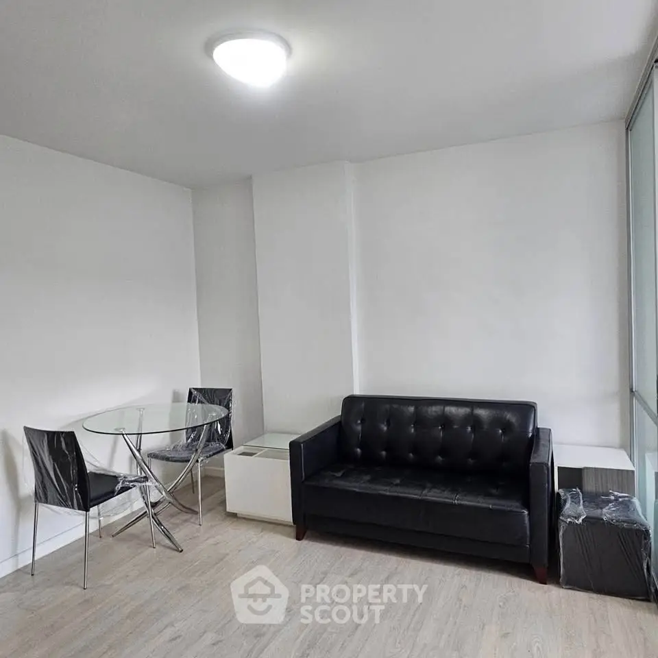 Modern living room with sleek black sofa and glass dining table in a minimalist design.