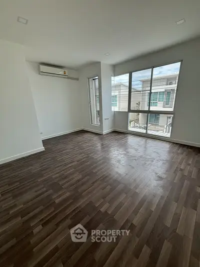 Spacious empty room with large windows and wooden flooring, perfect for customization.