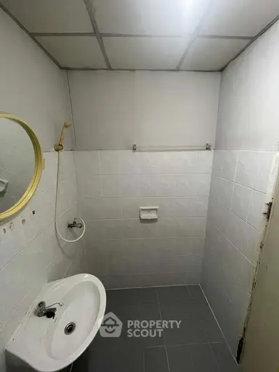 Compact bathroom with minimalist design and tiled walls, featuring a round mirror and basic fixtures.