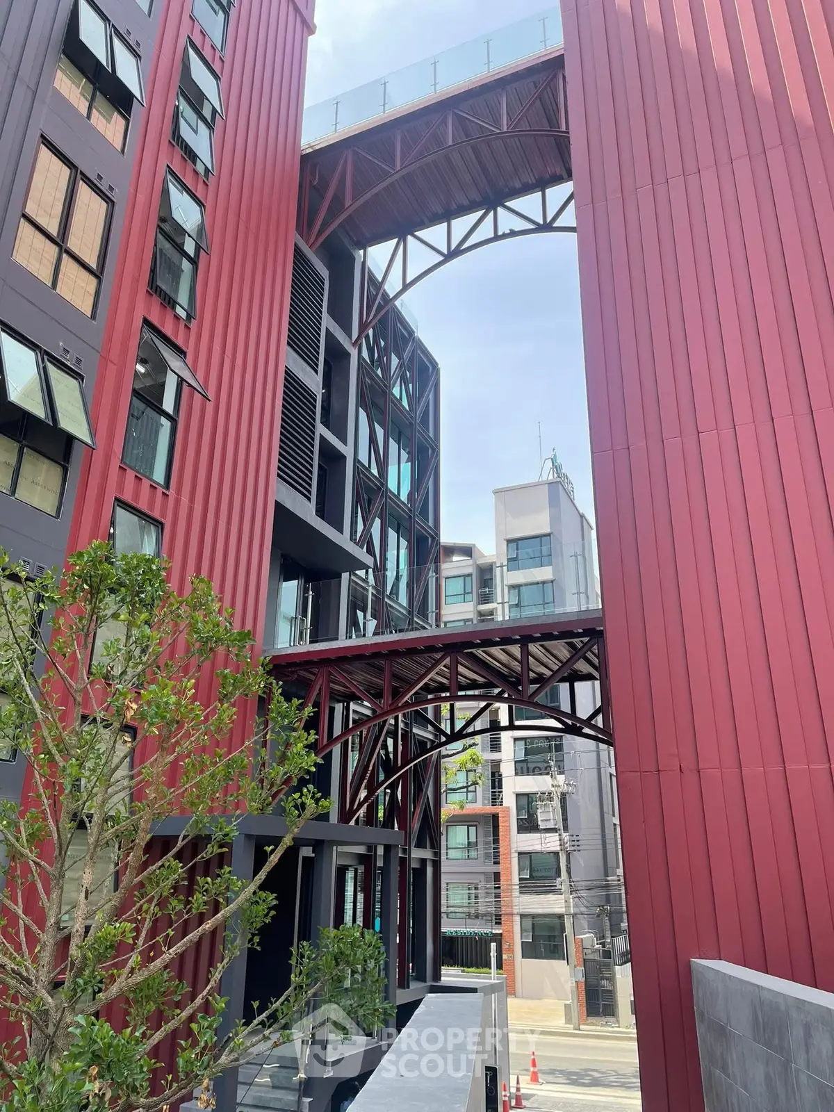 Modern architectural building with unique red facade and sky bridge in urban setting.