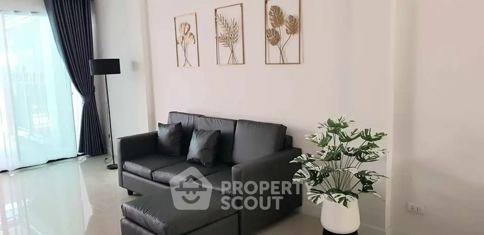 Modern living room with sleek black sofa, elegant decor, and natural light from large windows.