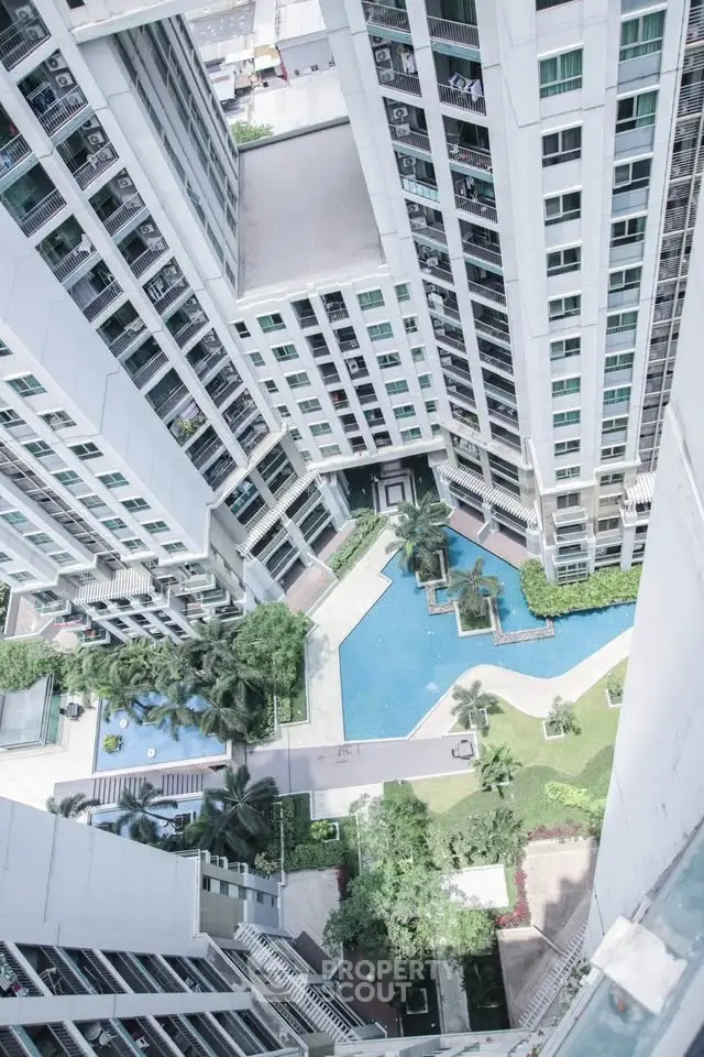 Stunning aerial view of modern high-rise building with luxurious pool and lush garden area.