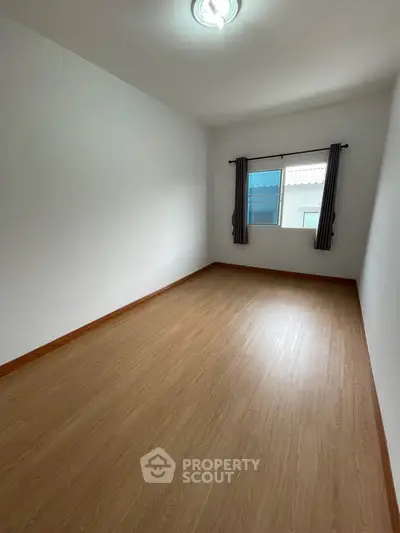 Spacious empty bedroom with wooden flooring and natural light