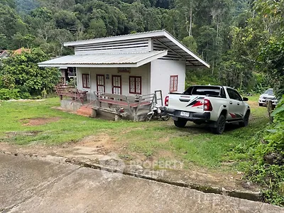Charming rural house with lush greenery and parked vehicles, perfect for nature lovers seeking tranquility.