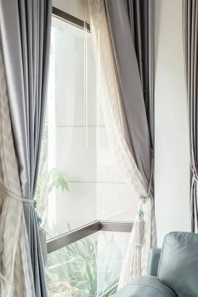 Elegant corner window with luxurious curtains and plush sofa in modern living room.