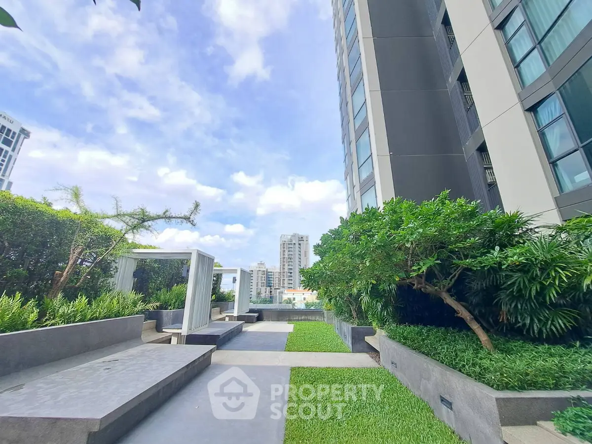 Modern urban garden with lush greenery and city views in a high-rise building complex.
