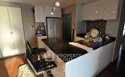 Modern kitchen with sleek black countertops and stylish bar stools in cozy apartment.