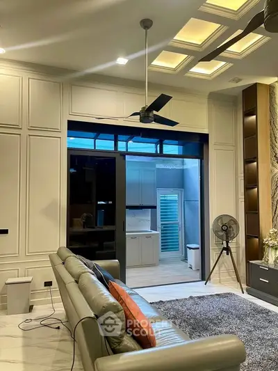 Luxurious living room with modern ceiling fan and stylish decor leading to a sleek kitchen area.