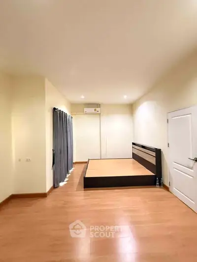 Spacious bedroom with wooden flooring and modern bed frame, featuring natural light and neutral tones.