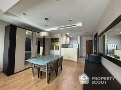 Spacious modern apartment with open layout connecting a sleek kitchen to an elegant dining area, featuring hardwood floors and contemporary lighting.