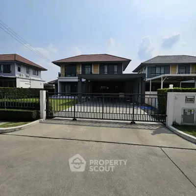 Modern two-story house with gated driveway and manicured lawn in suburban neighborhood.
