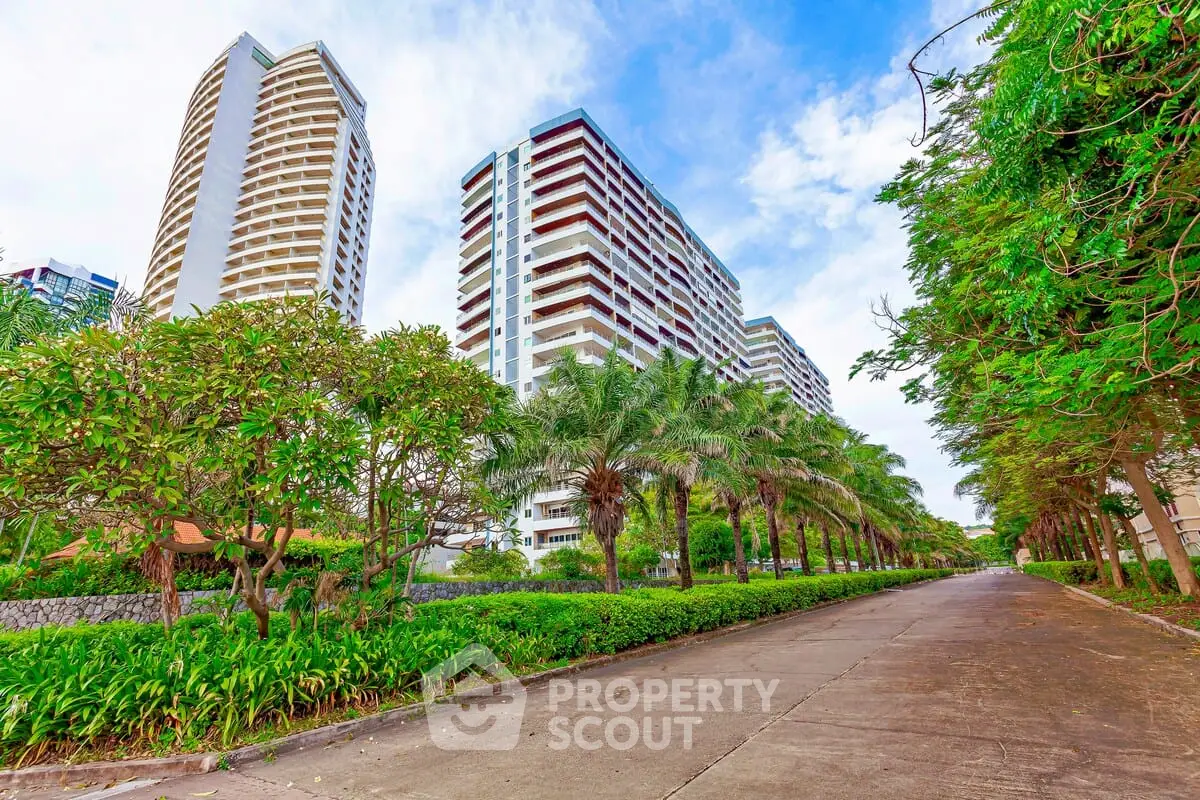 Luxurious high-rise building with lush greenery and palm-lined pathway in urban setting.