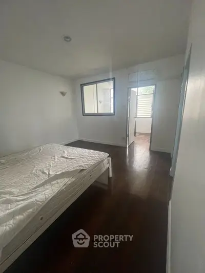 Cozy bedroom with dark wooden flooring and large window for natural light.