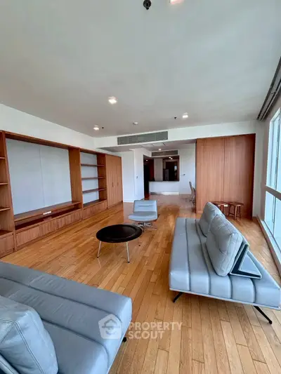 Spacious modern living room with sleek furniture and wooden flooring, featuring large windows for natural light.