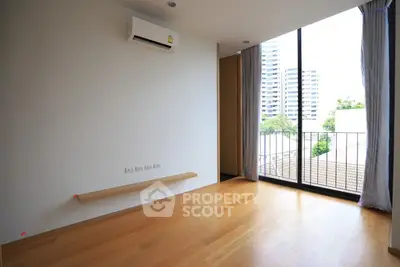 Spacious room with wooden flooring and large window offering city view, perfect for modern living.