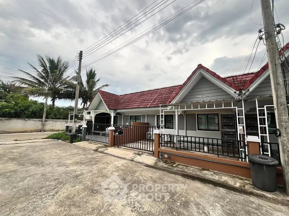 Charming suburban house with red roof and fenced yard under a cloudy sky.