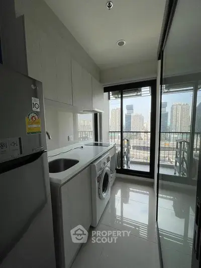 Modern kitchen with washing machine and city view from balcony in high-rise apartment.