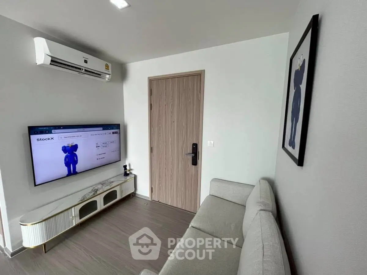 Modern living room with sleek furniture and wall-mounted TV, featuring minimalist decor and air conditioning.