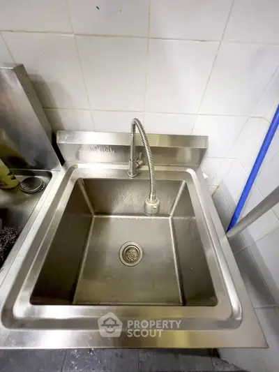 Stainless steel kitchen sink with modern faucet in a tiled kitchen setting.