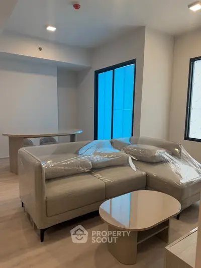 Modern living room with new furniture wrapped in plastic, featuring a stylish sofa and coffee table.