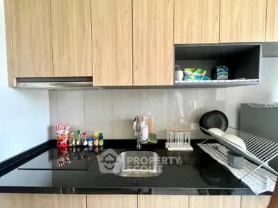 Modern kitchen with sleek black countertop and wooden cabinets, featuring an electric stove and sink.