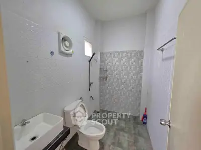 Spacious bathroom with modern fixtures and tiled walls, featuring a toilet, sink, and shower area.