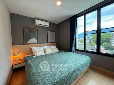 Modern bedroom with large window offering scenic city and mountain views, featuring stylish decor and cozy ambiance.