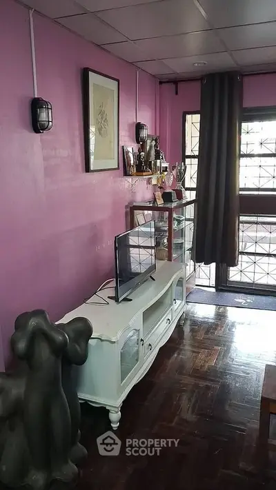 Charming living room with pink walls and stylish decor, featuring a TV stand and unique art pieces.