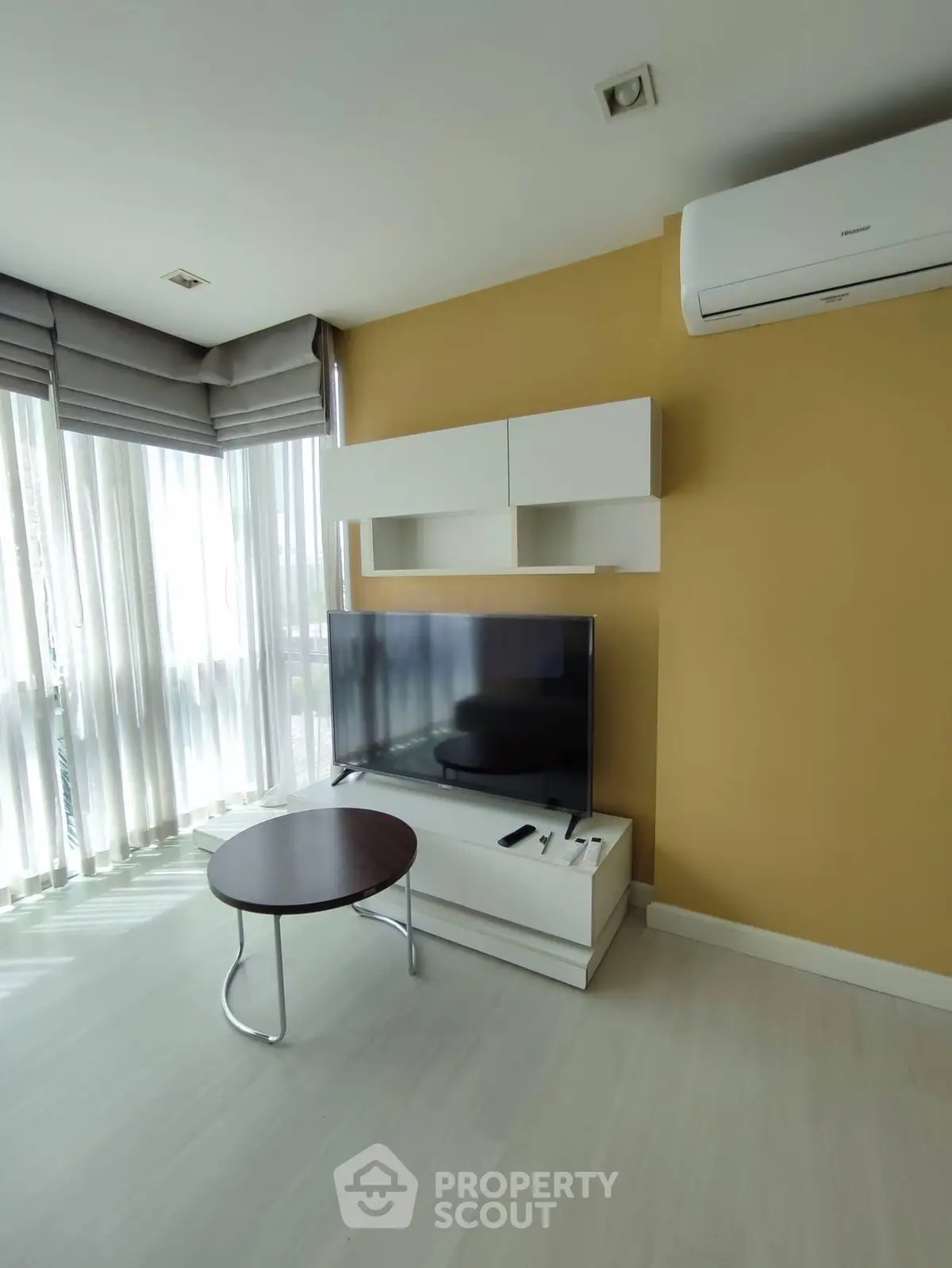 Modern living room with large TV, air conditioning, and natural light from floor-to-ceiling windows.