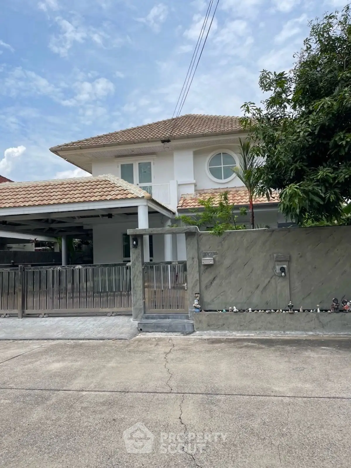 Charming two-story house with tiled roof and gated driveway in a serene neighborhood.