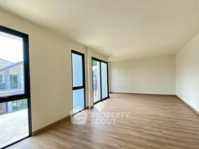 Spacious empty living room with large windows and wooden flooring, perfect for customization.