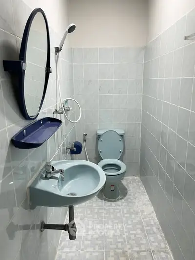 Compact bathroom with blue fixtures and tiled walls, featuring a round mirror and modern design.