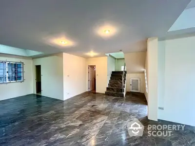 Spacious living area with polished marble flooring, ample natural light, and a staircase leading to the upper level, perfect for family gatherings and entertainment.