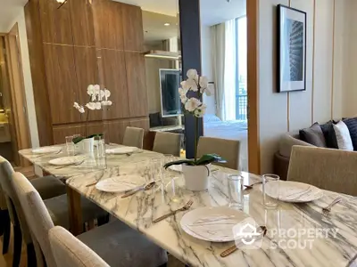 Elegantly set dining table in a modern open-plan living space with marble top, complemented by chic wooden cabinetry and plush seating area.