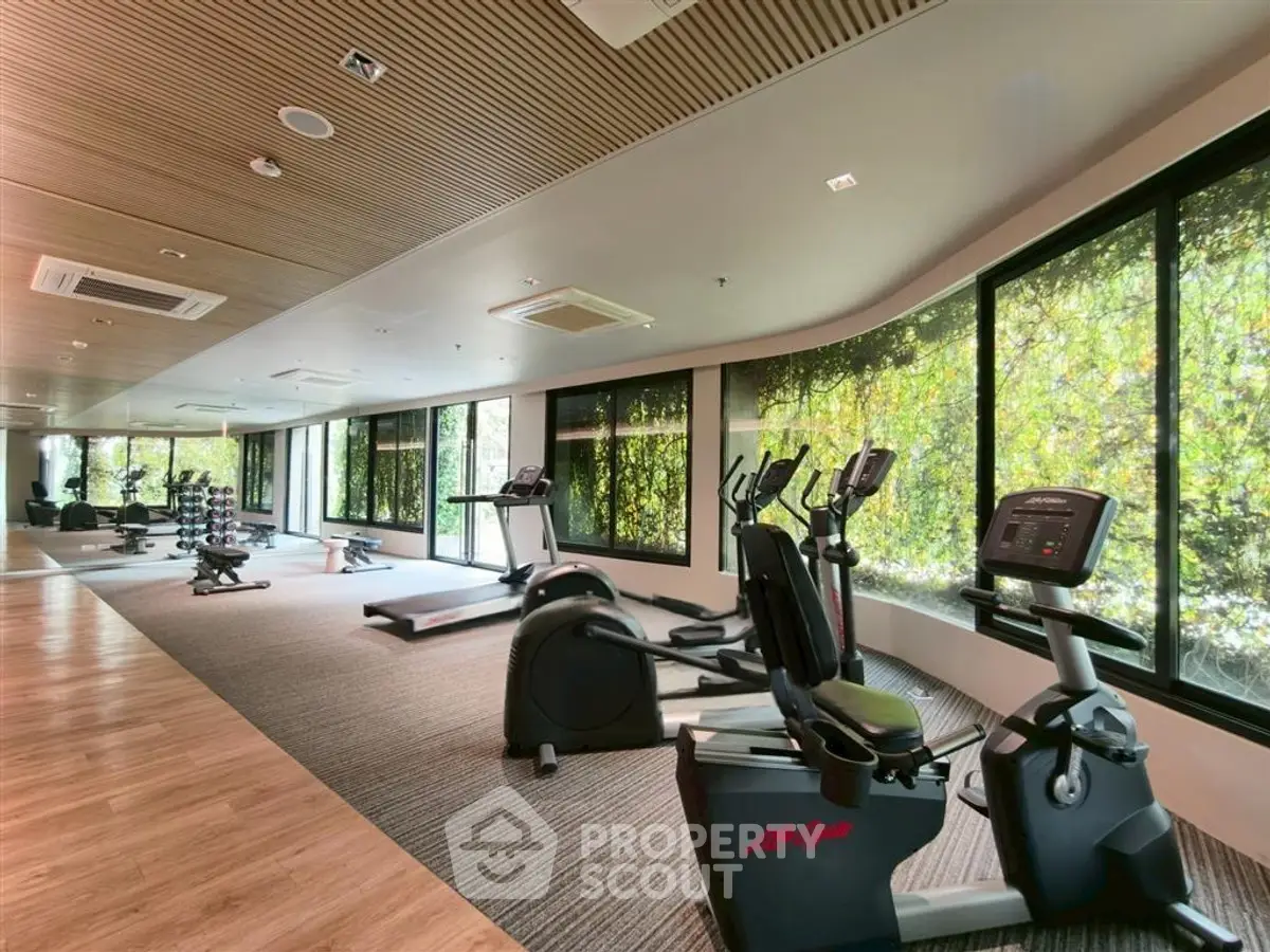 Spacious gym with modern equipment and large windows offering lush green views.
