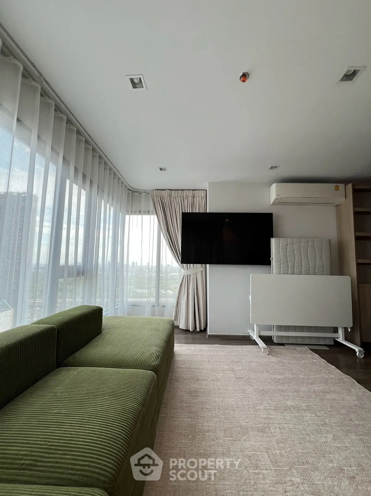 Spacious modern living room with large windows and green sofa, offering a bright and airy atmosphere.