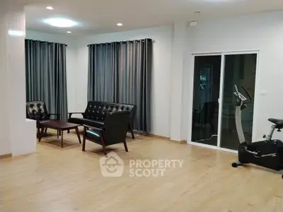 Spacious living room with modern furniture and exercise bike, featuring wooden flooring and large windows.