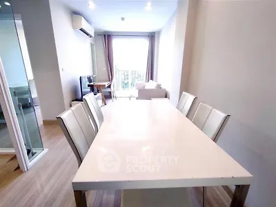 Modern dining area with sleek white table and chairs, open layout to living room with natural light.