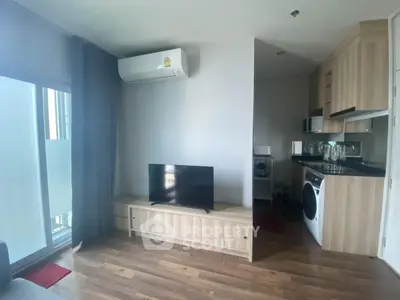 Modern apartment living room with TV and compact kitchen featuring washing machine