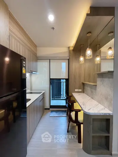 Modern kitchen with sleek design and balcony view, featuring stylish lighting and wooden accents.