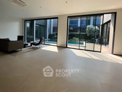 Spacious living room with large windows overlooking a private pool and garden, offering a luxurious and serene ambiance.