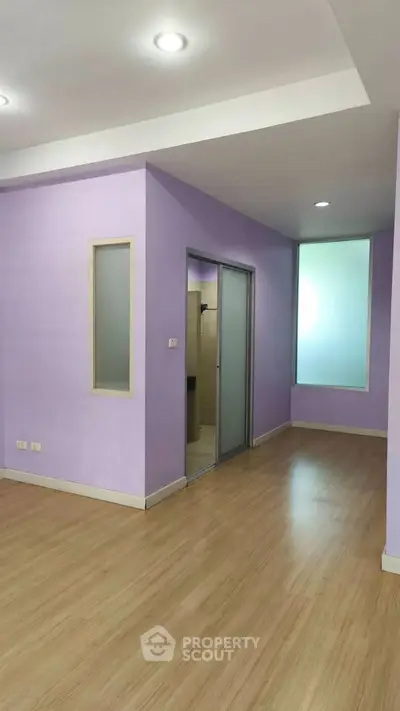Spacious modern room with purple walls and wooden flooring, featuring recessed lighting and a sliding door.