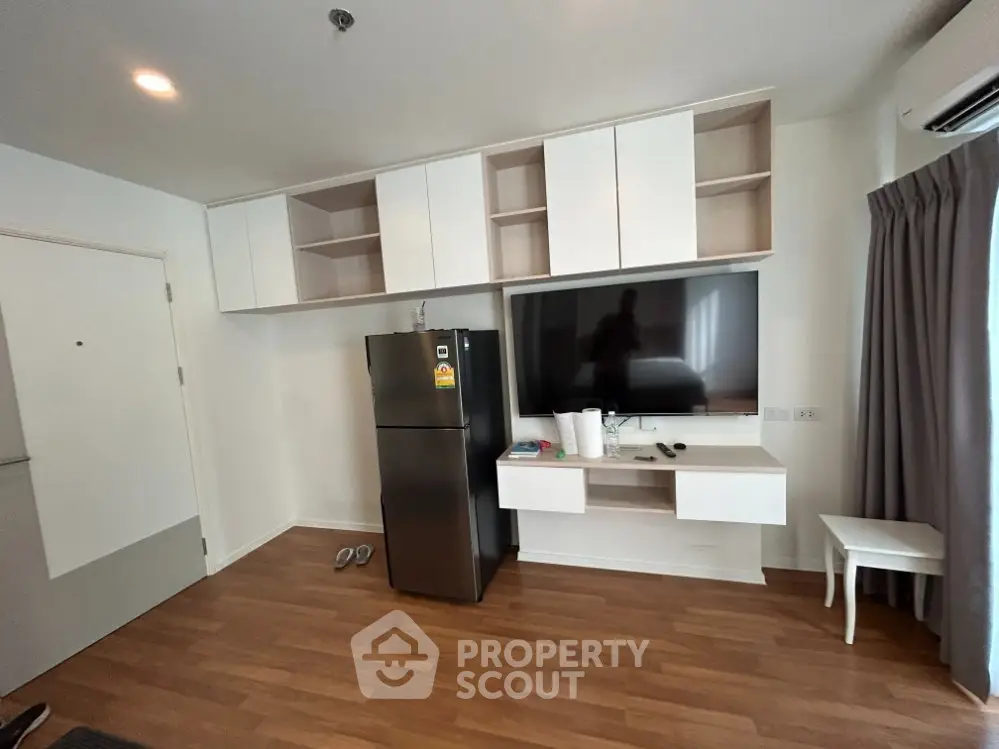 Modern living room with sleek cabinetry and large TV, featuring a stylish black refrigerator and elegant wood flooring.