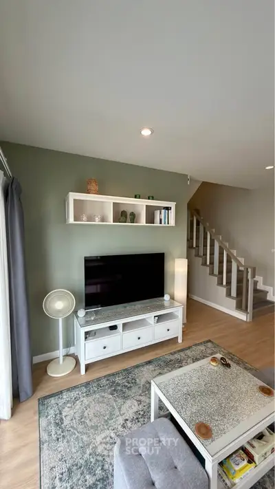 Modern living room with stylish decor and staircase, featuring a large TV and elegant shelving.